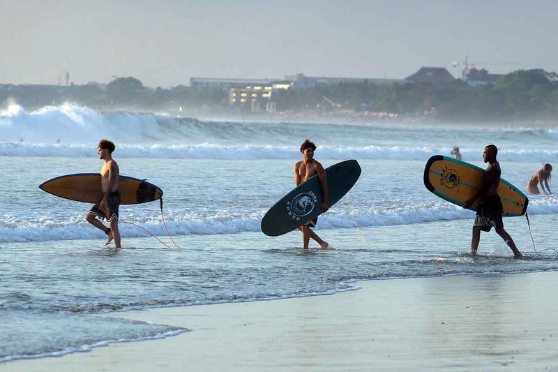 Sejumlah wisatawan membawa papan selancar berjalan menuju ke tengah laut saat berlibur di Pantai Kuta, Badung, Bali, Senin (25/9/2023). Kepala Dinas Pariwisata Provinsi Bali Tjok Bagus Pemayun mengatakan untuk retribusi sebesar Rp150 ribu kepada turis asing yang masuk Pulau Dewata diterapkan mulai Februari 2024 dan mekanismenya serta tata cara pungutan uang kepada turis asing hingga saat ini masih disusun dalam Peraturan Gubernur (Pergub) Bali. ANTARA FOTO/Nyoman Hendra Wibowo