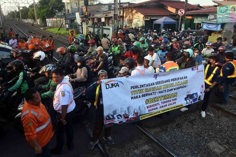 Petugas KAI Commuter bersama relawan membentangkan spanduk saat sosialisasi keselamatan perkeretaapian di perlintasan sebidang Stasiun Pondok Jati, Jakarta, Rabu (27/9/2023). Dalam rangka memperingati Hari Perhubungan Nasional, KAI Commuter melakukan kampanye keselamatan di perlintasan sebidang guna meningkatkan kesadaran para pengguna jalan raya untuk mendahulukan perjalanan kereta api yang akan melintas dan tidak menerobos palang pintu perlintasan. ANTARA FOTO/Indrianto Eko Suwarso