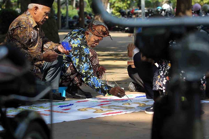 Anggota komunitas sepeda tua Senopati melukis batik pada selembar kain saat Hari Bebas Kendaraan Bermotor di Jalan Darmo, Surabaya, Jawa Timur, Minggu (1/10/2023). Kegiatan melukis batik bersama dengan mengenakan busana batik tersebut untuk melestarikan warisan budaya tak benda dari Indonesia sekaligus menyambut Hari Batik Nasional yang diperingati setiap tanggal 2 Oktober. ANTARA FOTO/Didik Suhartono